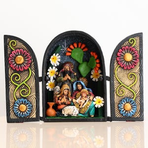 May include: A colorful, hand-painted nativity scene in a triptych style. The central arched panel depicts the holy family, surrounded by flowers and cacti. The side panels feature large, stylized flowers in pink, blue, and yellow.