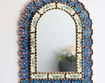 May include: An arched wall mirror with a blue, gold, and cream floral design. The mirror's frame has a scalloped edge with blue and gold accents. The central section features a cream-colored border with floral patterns, and the mirror reflects a room.