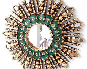 May include: A gold sunburst mirror with a green and white tiled center. The mirror has a round shape and is surrounded by a decorative frame.