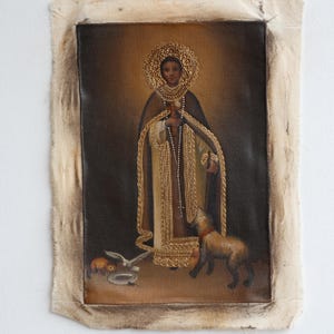 Könnte beinhalten: Antikes religiöses Gemälde auf Leinwand. Das Kunstwerk zeigt eine Figur mit goldenem Heiligenschein, die ein Kreuz und Rosenkranzperlen hält. Ein Hund und andere Tiere befinden sich zu Füßen der Figur. Das Gemälde ist mit einem verwitterten, gealterten Rahmen versehen.