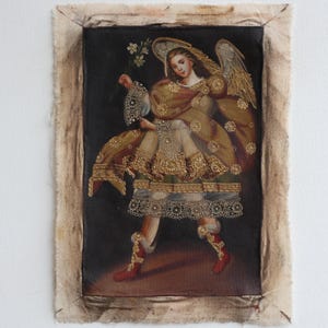 May include: An antique painting of an angel with golden wings, holding flowers. The angel wears a gold and brown gown with intricate lace and floral details, and red boots. The artwork is framed with a raw, textured border.