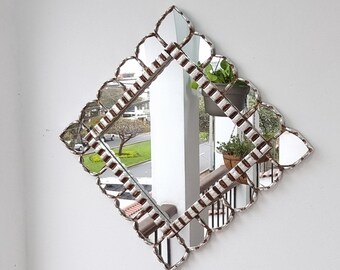 Op de afbeelding: Een ruitvormige spiegel met een decoratief frame gemaakt van kleine, overlappende stukjes glas. Het frame is zilver en bruin met een wit en bruin gestreept patroon. De spiegel reflecteert een uitzicht op een balkon met planten en een straat.