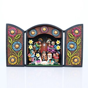 May include: A hand-carved, wooden nativity scene with a triptych design. The central scene depicts the holy family, surrounded by figures in colorful clothing. The frame is decorated with floral patterns in pink, blue, and yellow.