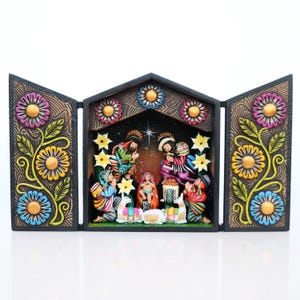 May include: A hand-painted, wooden nativity scene with a triptych design. The central scene depicts the holy family and the three wise men. The frame is decorated with colorful flowers and foliage. The color palette includes brown, black, blue, yellow, and pink.