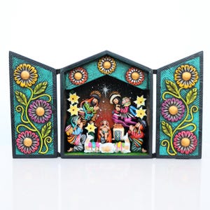 May include: A hand-painted, three-panel nativity scene. The central panel depicts the holy family with figures in colorful clothing. The side panels feature floral designs with yellow, pink, and purple flowers on a teal background.