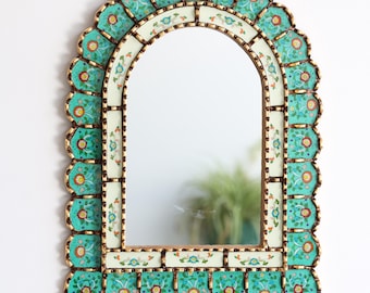 May include: An arched wall mirror with a decorative frame. The frame features a scalloped edge with turquoise and gold accents, and floral patterns. The mirror's interior is a reflective surface.