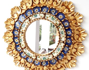 May include: A round mirror with a gold frame decorated with blue and white floral tiles. The frame is intricately carved with a sunburst design.