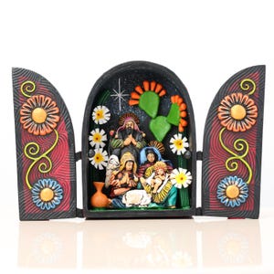 May include: A colorful, hand-painted nativity scene. The central arched frame features a star, cactus, and figures. The side panels have floral designs in orange, yellow, and blue. The overall design is a folk art style.