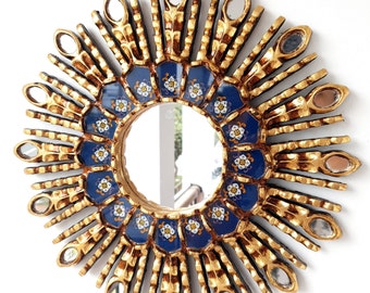 May include: A gold sunburst mirror with a blue and white tile design. The mirror is round and has a decorative frame.