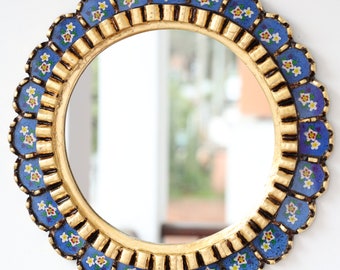 May include: A round mirror with a gold frame and a blue and white floral design. The mirror has a scalloped edge and is perfect for adding a touch of elegance to any room.
