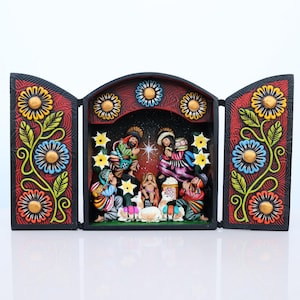 May include: A three-panel, hand-carved nativity scene. The central panel depicts the holy family and onlookers, while the side panels feature floral designs in yellow, blue, and orange against a red background. The artwork is detailed and colorful.