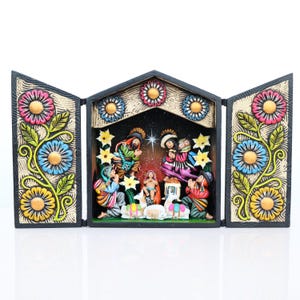 May include: A hand-painted, wooden nativity scene with a triptych design. The central scene depicts the holy family and onlookers, with colorful figures and a starry backdrop. The frame is decorated with floral patterns in shades of pink, blue, and yellow.
