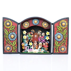 May include: A carved wooden nativity scene with a central panel and two side panels. The panels are black with colorful floral designs. The central scene depicts figures in vibrant clothing, with a star above. The overall color scheme is red, black, and various bright colors.