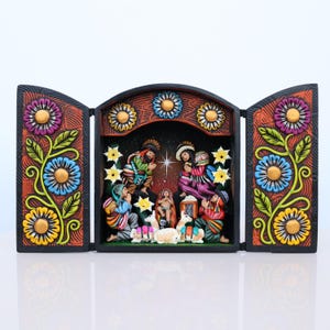 May include: A three-panel, hand-carved nativity scene. The central panel depicts the holy family and the three wise men. The side panels feature colorful floral designs with blue, yellow, and purple flowers. The frame is black.