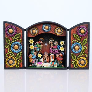 May include: A three-panel, hand-carved nativity scene. The black frame is decorated with colorful flowers and foliage. The central panel depicts the holy family and surrounding figures. The figures are dressed in vibrant clothing.
