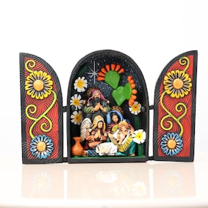 May include: A hand-painted, three-panel nativity scene. The central panel depicts the holy family with figures in colorful robes. The side panels feature floral designs in yellow, blue, and red. The background is black with white stars.