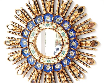 May include: A gold sunburst mirror with a blue and white tile design. The mirror has a round shape and is surrounded by a decorative frame.