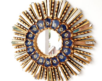 May include: A gold sunburst mirror with a blue and white tile design around the mirror. The mirror is round and has a gold frame.