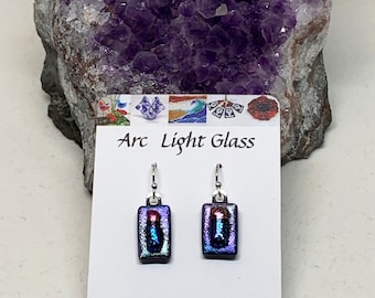 May include: A pair of iridescent purple and blue glass rectangle earrings with silver hooks. The earrings are displayed on a white card with the text "Arc Light Glass" and "www.arclightglass.etsy.com".