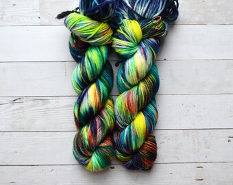 Op de afbeelding: Twee bollen garen in een felle groen, geel, blauw en zwarte kleur. Het garen is gedraaid in een touwvorm.