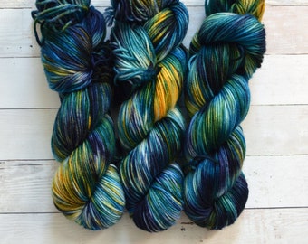 Op de afbeelding: Drie bollen garen in tinten van blauw, groen en geel. Het garen is handgeverfd en heeft een gevarieerd kleurpatroon.