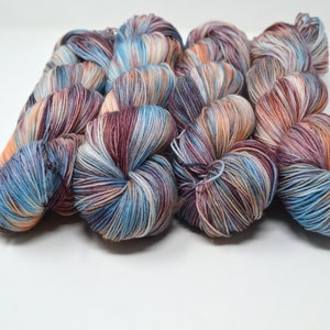 May include: A skein of hand-dyed yarn in shades of blue, white, orange, and brown. The yarn is arranged in a pile, showing the different colour variations.