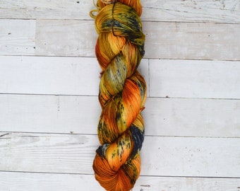 May include: A skein of yarn in a mix of orange, yellow, black, and blue colors. The yarn is arranged in a spiral shape.