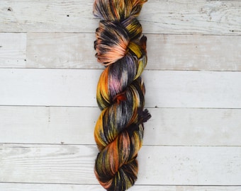 May include: A skein of yarn in a multi-colored pattern of black, orange, yellow, and pink. The yarn is twisted into a rope shape.