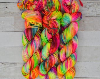 May include: Three skeins of brightly coloured yarn in shades of pink, orange, yellow, green, blue, and purple. The yarn is twisted together in a spiral pattern.