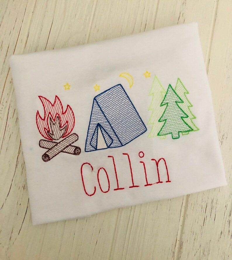 May include: A white t-shirt with an embroidered design of a campfire, tent, and pine trees. The name "Collin" is embroidered below the design in red thread.