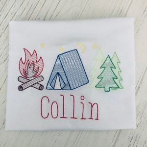 May include: Embroidered design on a white t-shirt featuring a red campfire, a blue tent, two green trees, and the name "Collin" in red.