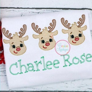 May include: White embroidered shirt with three red-nosed reindeer faces and the name "Charlee Rose" stitched in green thread.