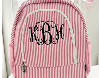 May include: A pink and white vertical striped quilted backpack featuring a large black monogram with the letters KBH in a decorative script font. The bag includes a front zippered pocket with a white trim, a top handle, and side mesh pockets.