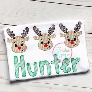 May include: White onesie with three embroidered reindeer faces and the name "Hunter" in green lettering.