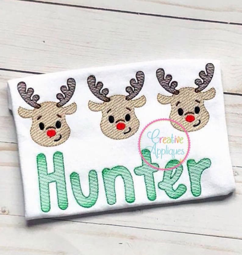 May include: White onesie with three embroidered reindeer faces and the name "Hunter" in green lettering.