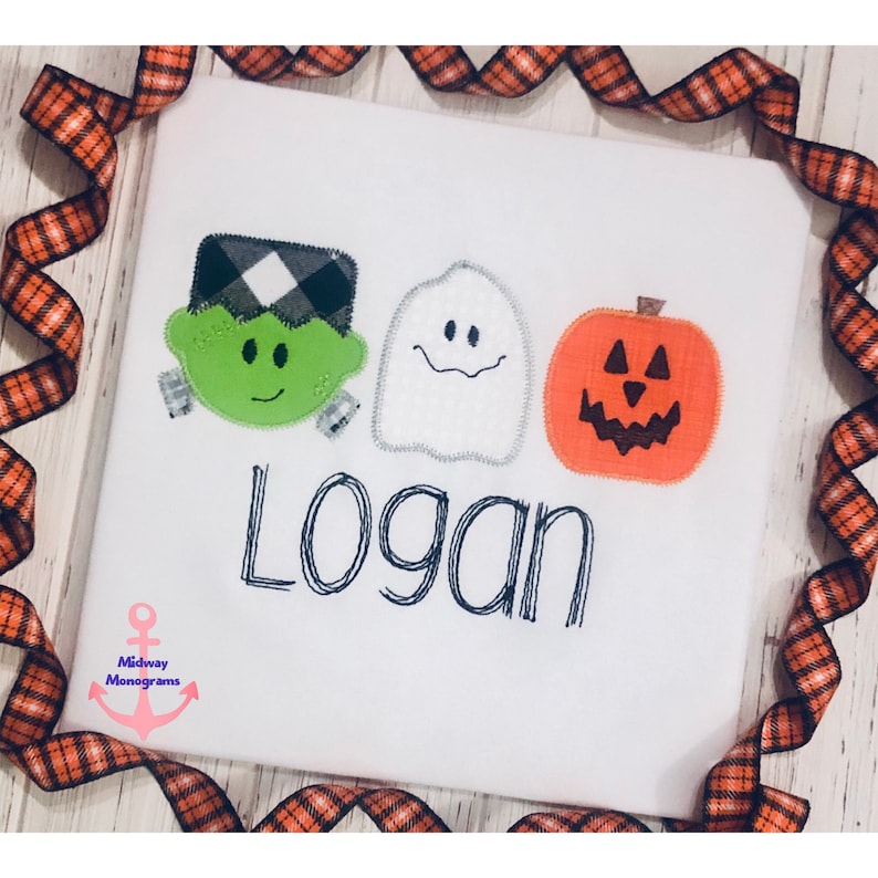 May include: White t-shirt featuring a green Frankenstein, a white ghost, and an orange pumpkin with a jack-o-lantern face. The name "Logan" is embroidered in black below the characters.