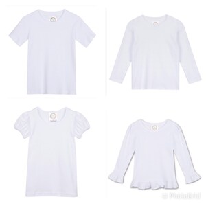 May include: Four white t-shirts for kids. Two short-sleeved t-shirts and two long-sleeved t-shirts. One long-sleeved t-shirt has a ruffle trim.
