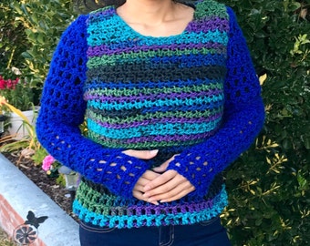 May include: A woman wearing a blue and green striped crochet sweater with blue crochet sleeves. The sweater has a round neckline and a loose fit.