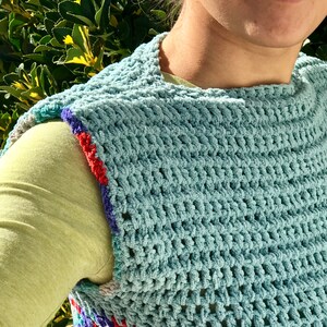 May include: A light blue crochet vest with a colorful trim around the armholes. The vest is made with a textured stitch and has a loose, open weave.