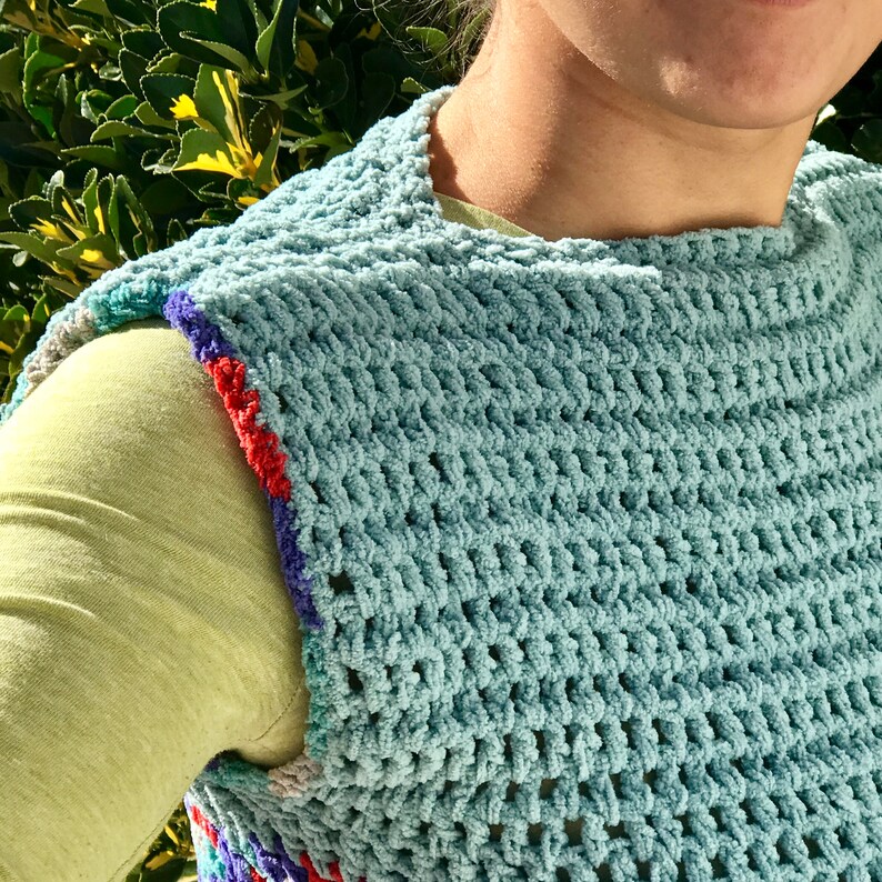 May include: A light blue crochet vest with a colorful trim around the armholes. The vest is made with a textured stitch and has a loose, open weave.