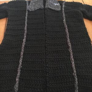 Puede incluir: Un c&aacute;rdigan de ganchillo negro con un cuello de piel sint&eacute;tica gris. El c&aacute;rdigan tiene una abertura delantera larga y est&aacute; hecho con un punto texturizado.