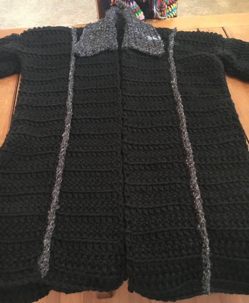 Puede incluir: Un c&aacute;rdigan de ganchillo negro con un cuello de piel sint&eacute;tica gris. El c&aacute;rdigan tiene una abertura delantera larga y est&aacute; hecho con un punto texturizado.