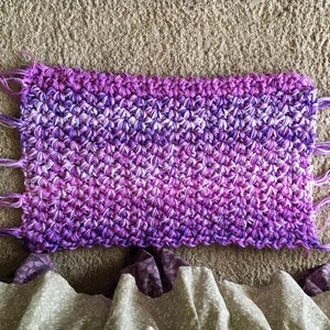 May include: A purple and white crocheted throw blanket with fringe on all sides.