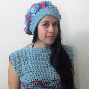 May include: A woman wearing a blue and red crocheted beret and a matching blue crocheted top.