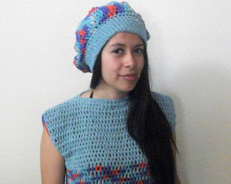 May include: A woman wearing a blue and red crocheted beret and a matching blue crocheted top.