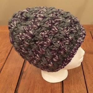 Puede incluir: Un gorro de punto de color gris y morado con hilo blanco tejido.