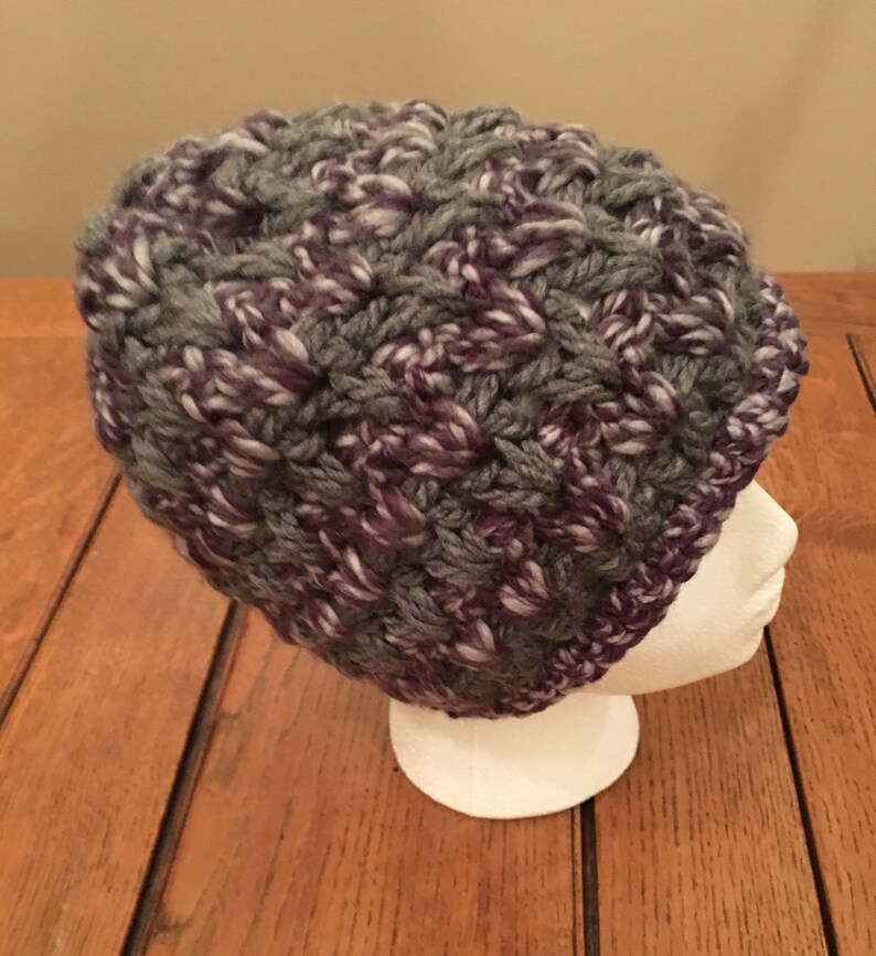 Puede incluir: Un gorro de punto de color gris y morado con hilo blanco tejido.