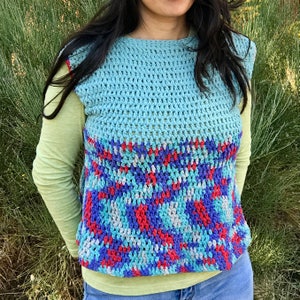 May include: A sleeveless crochet vest with a blue, red, and white geometric pattern. The vest is crocheted in a textured stitch and has a loose fit.