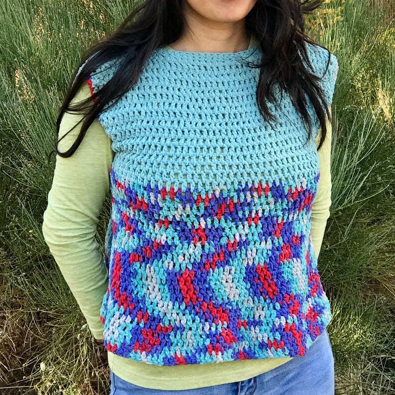 May include: A sleeveless crochet vest with a blue, red, and white geometric pattern. The vest is crocheted in a textured stitch and has a loose fit.