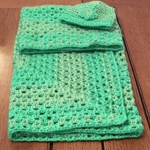 May include: A green crocheted baby blanket with a matching hat. The blanket is made with a textured stitch and has a gradient of green shades.